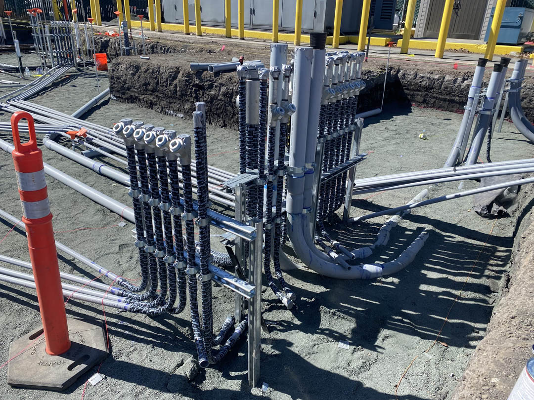 Conduit runs feeding upright electrical stubs at an outdoor equipment pad