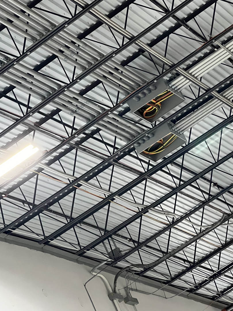 Overhead conduit and high-bay lighting across a warehouse ceiling
