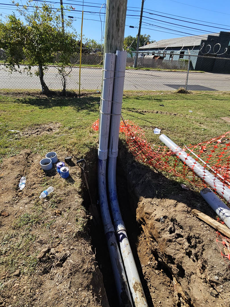Electrical conduits rising from a trench near a utility pole